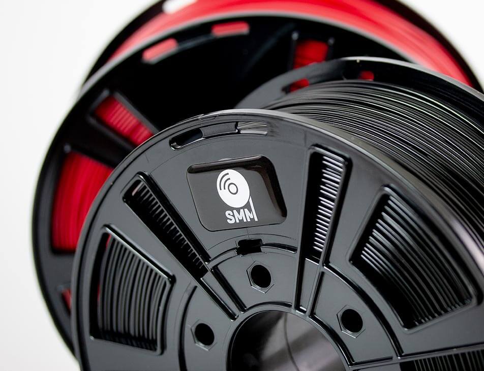 Two spools of 3D printing filaments, red and black with Smart Material Manager NFC tag on in.