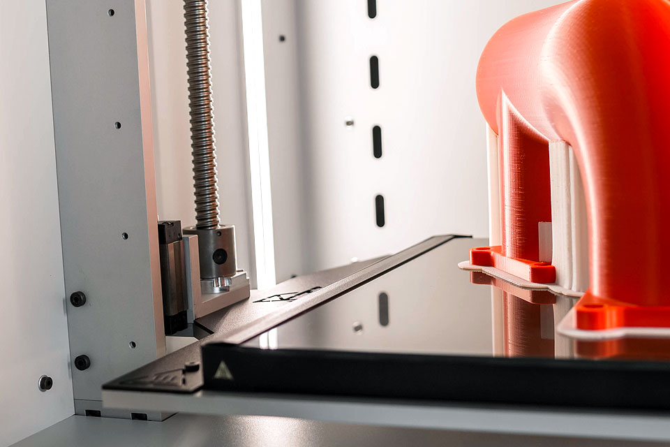 Przemysłowa drukarka 3D INDUSTRY F340. Czerwony wydruk 3d w komorze drukarki.