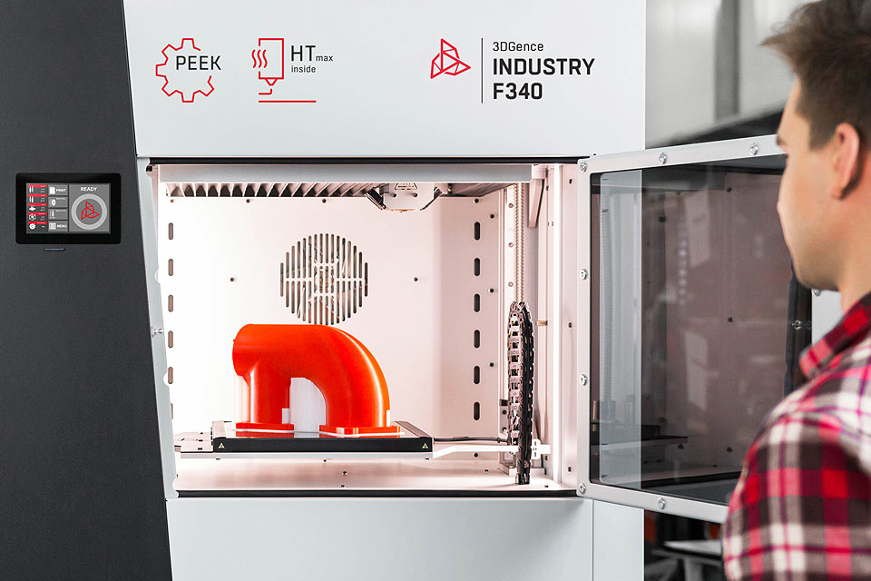 Industrial 3D printer INDUSTRY F340. Man standing in front of the printer. Open printing chamber and red printout inside.